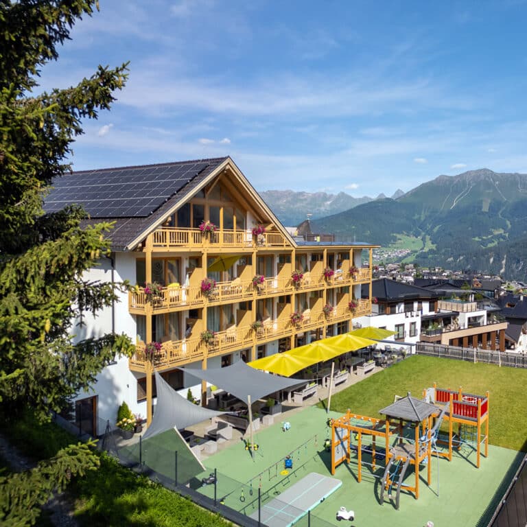 Hotel Natürlich in Fiss, Tirol. Anischt West im Sommer mit Terrasse und Spielplatz.
